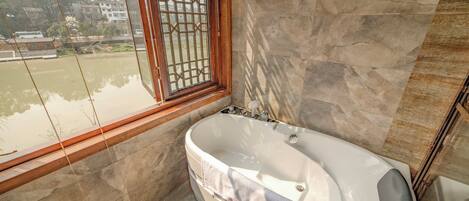 A bathroom with a bathtub, a window with a metal grille, and stone walls.