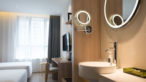 Ett modernt hotellrum med två sängar, ett badrum med handfat och spegel samt en TV.