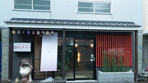 A building with a traditional tiled facade, a modern entrance with a glass door, and a small outdoor area with a decorative statue and plants. - Asakusa No Yado Hanaakari (Tokyo)
