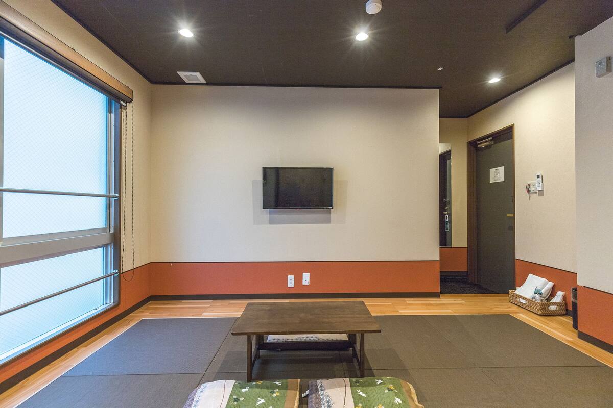 Habitación de hotel con un ventanal grande, un televisor de pantalla plana montado en la pared, una mesita pequeña y un banco.