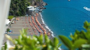 A beach with rows of umbrellas and sun loungers, a rocky coastline, and a building with a glass roof overlooking the beach. - Casa Noemi 4+2, Emma Villas (Positano)