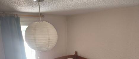 Una cama individual con estructura de madera y ropa de cama blanca en una habitación con techo texturizado y una ventana con cortinas.