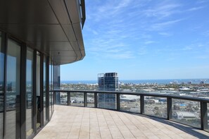Un edificio moderno con amplios ventanales y un balcón que ofrece vistas a un paisaje urbano y al mar.