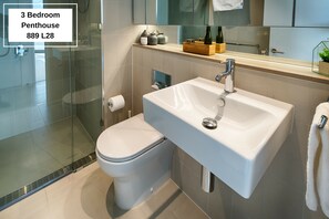 Baño de un ático de tres habitaciones, con cabina de ducha de vidrio, lavabo blanco y un inodoro.
