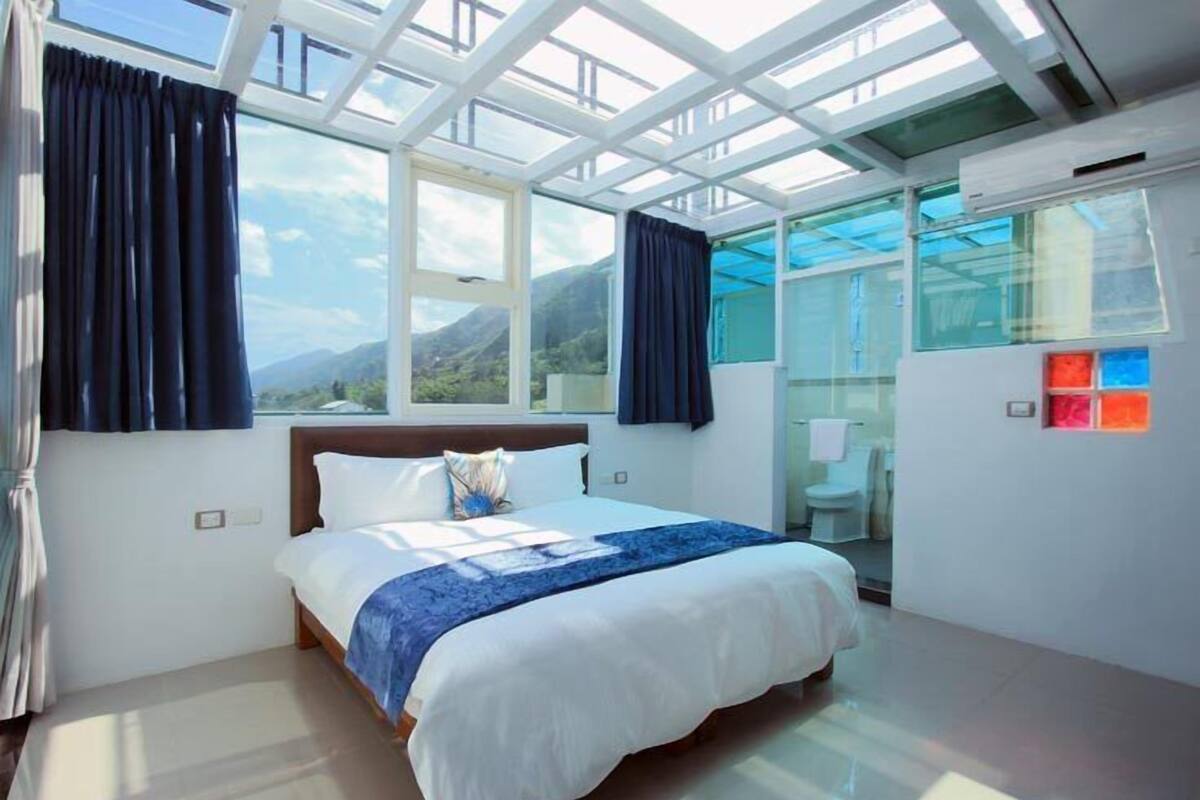 A bedroom with a large bed, a skylight, and a view of mountains.