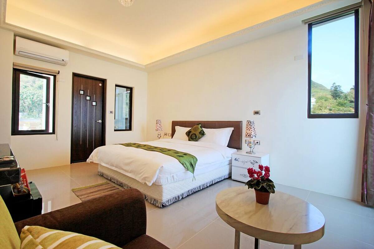 A bedroom with a bed, bedside tables, a round table, and a window with a view.