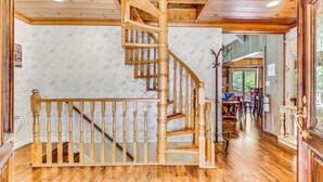 A wooden staircase leading to a second floor, a dining area with a table and chairs, and a view of the outdoors through a window.