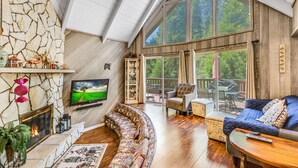 A spacious living room with a stone fireplace, a large TV, and a cozy seating area with a blue sofa and a curved sectional.