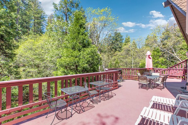 Une terrasse extérieure couverte, dotée de tables et de chaises en métal, entourée d’une rambarde rouge et offrant une vue sur une zone boisée.