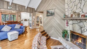 A spacious living area with a fireplace, wooden floors, and a herringbone-patterned stone wall.