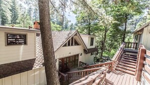 A cabin with a wooden deck, a staircase, and a view of the surrounding forest.