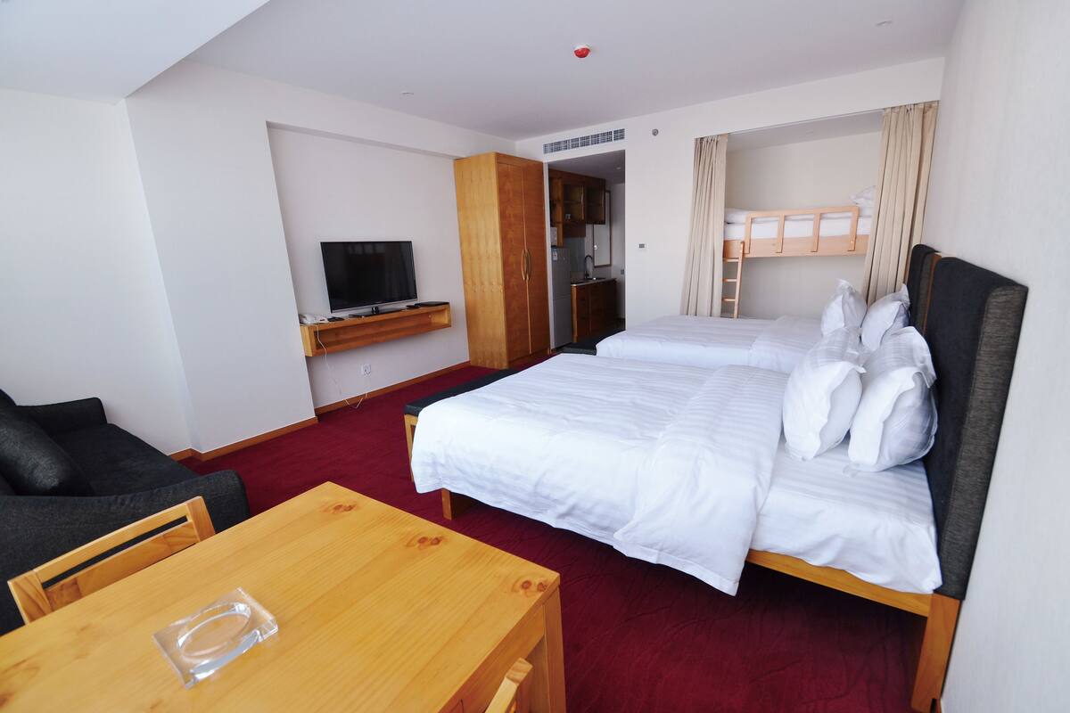 A hotel room with a single bed, a TV, a wooden table, and a red carpet.