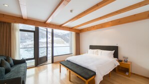 A bedroom with a bed, bench, nightstand, and a view of a snowy landscape through large windows. - Genting Grand Chongli (Zhangjiakou)