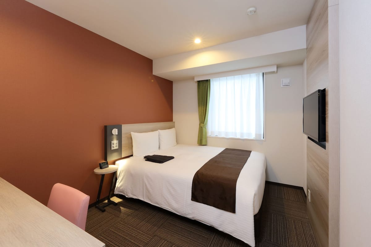 A hotel room with a bed, a desk, a chair, a TV, and a window with curtains.