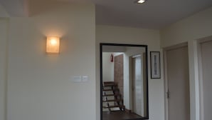 A hallway with a large mirror, a light fixture, and a door leading to a staircase. - Lazimpat House B&B (Kathmandu)