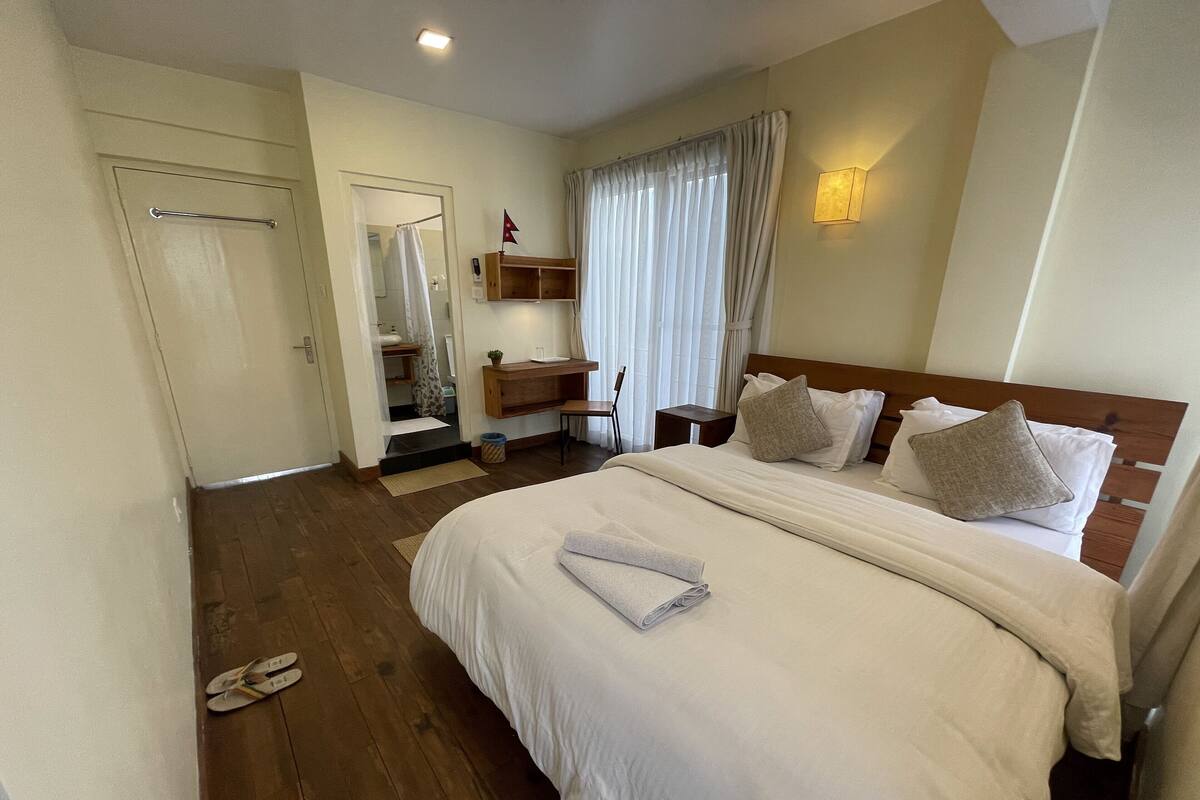 A hotel room with a large bed, a wooden headboard, a bedside table, a mirror, and a window with curtains.