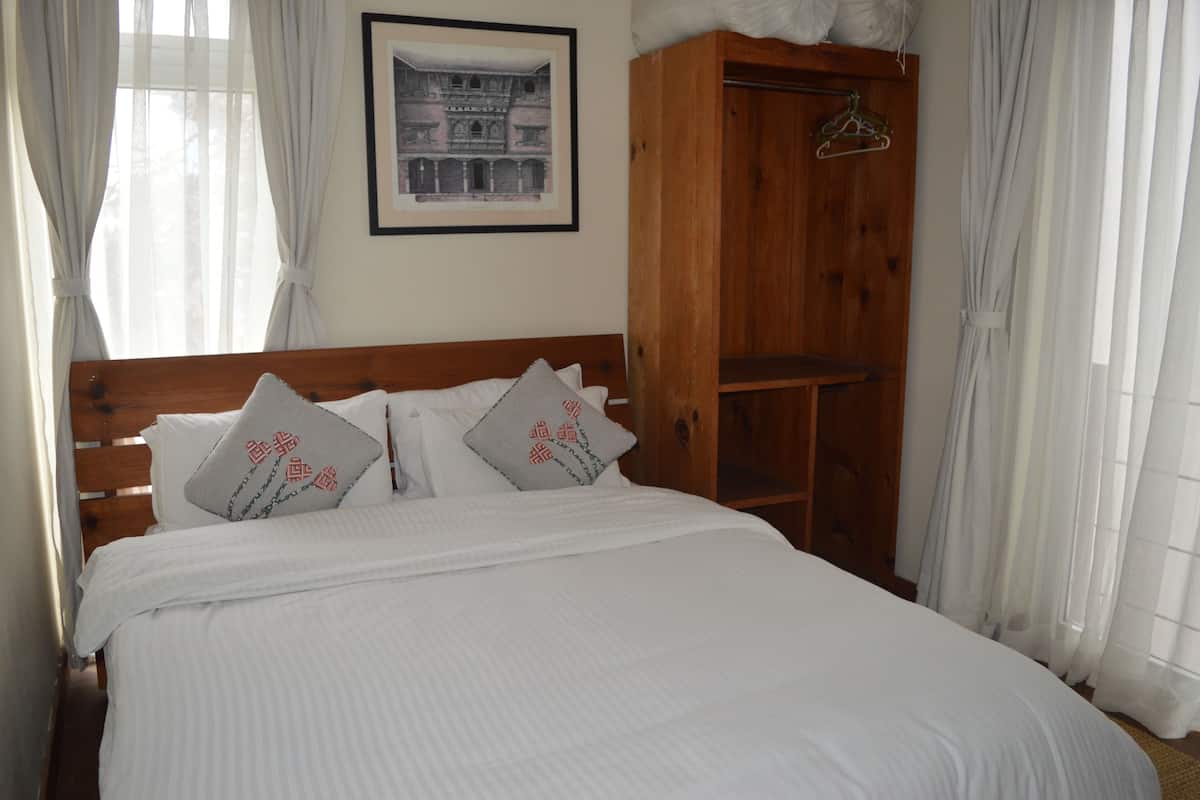 A neatly made bed with white bedding and two pillows with red text, a wooden wardrobe, and a framed picture on the wall.
