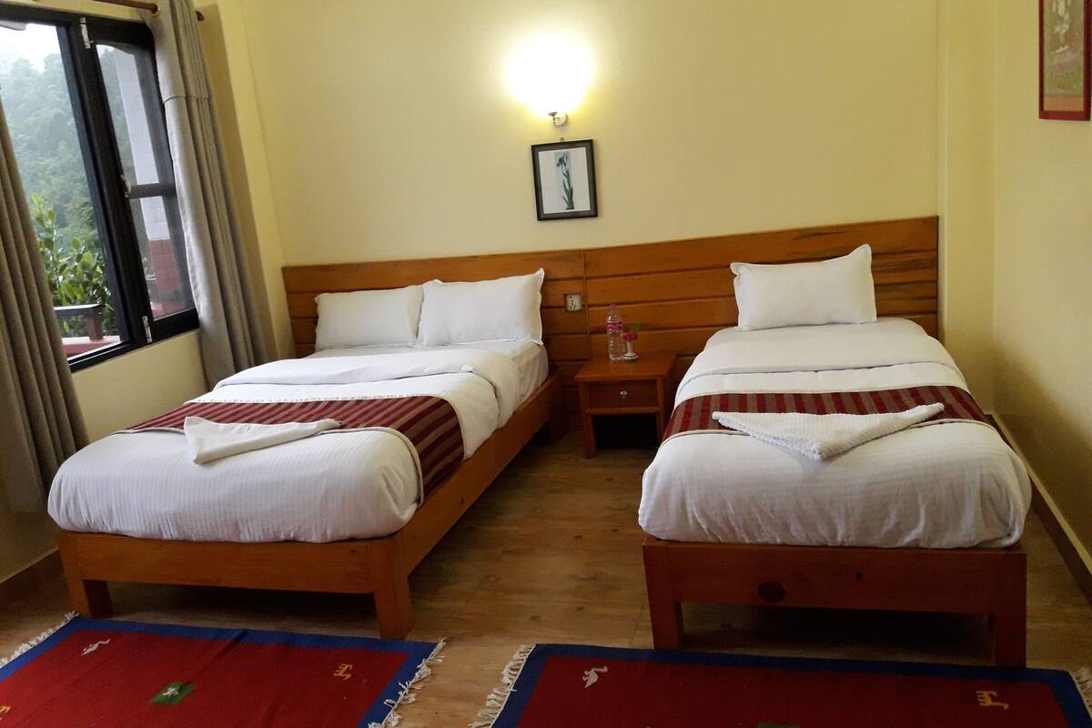 Una habitación de hotel con dos camas individuales, una mesita de noche, una lámpara de pared y una ventana con cortinas.