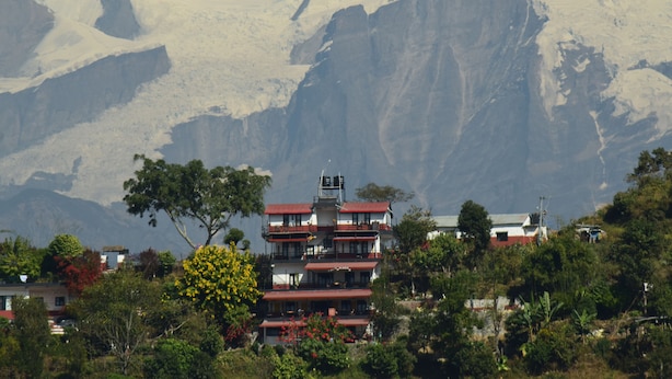 A multi-story building with balconies, surrounded by lush greenery and mountains in the background. - Siddhartha Garden (Pokhara)