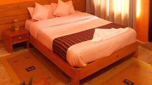 A hotel room with a wooden bed, a nightstand, and a window with curtains. - Siddhartha Garden (Pokhara)