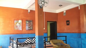 A room with orange and blue walls, a black and white striped sofa, a wicker chair, and a ceiling fan. - Siddhartha Garden (Pokhara)
