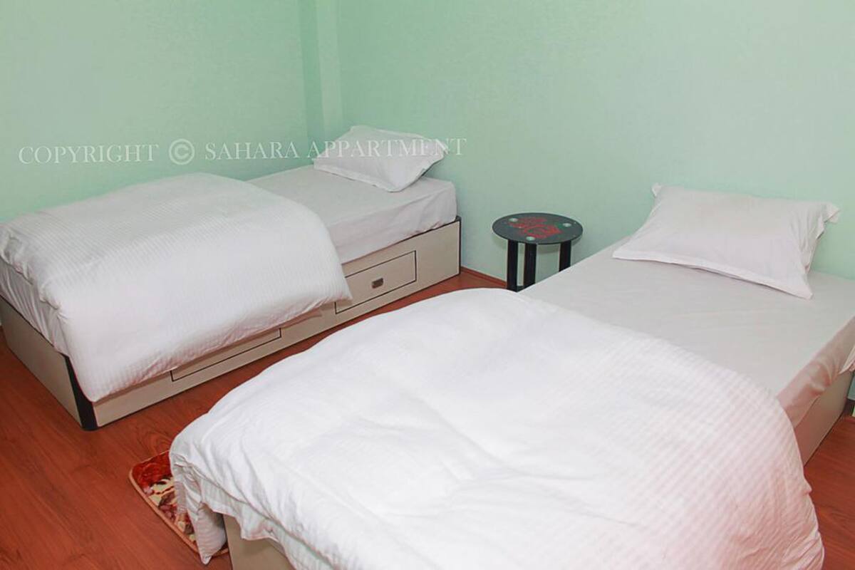 A room with two beds, each with white bedding and pillows, a small round table, and a wooden floor.