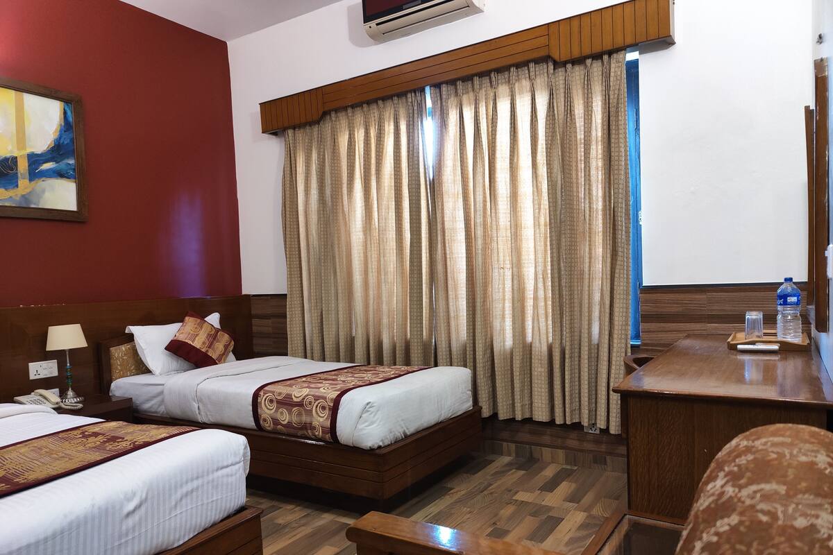 A hotel room with two beds, a desk, a chair, a telephone, and a painting on the wall.