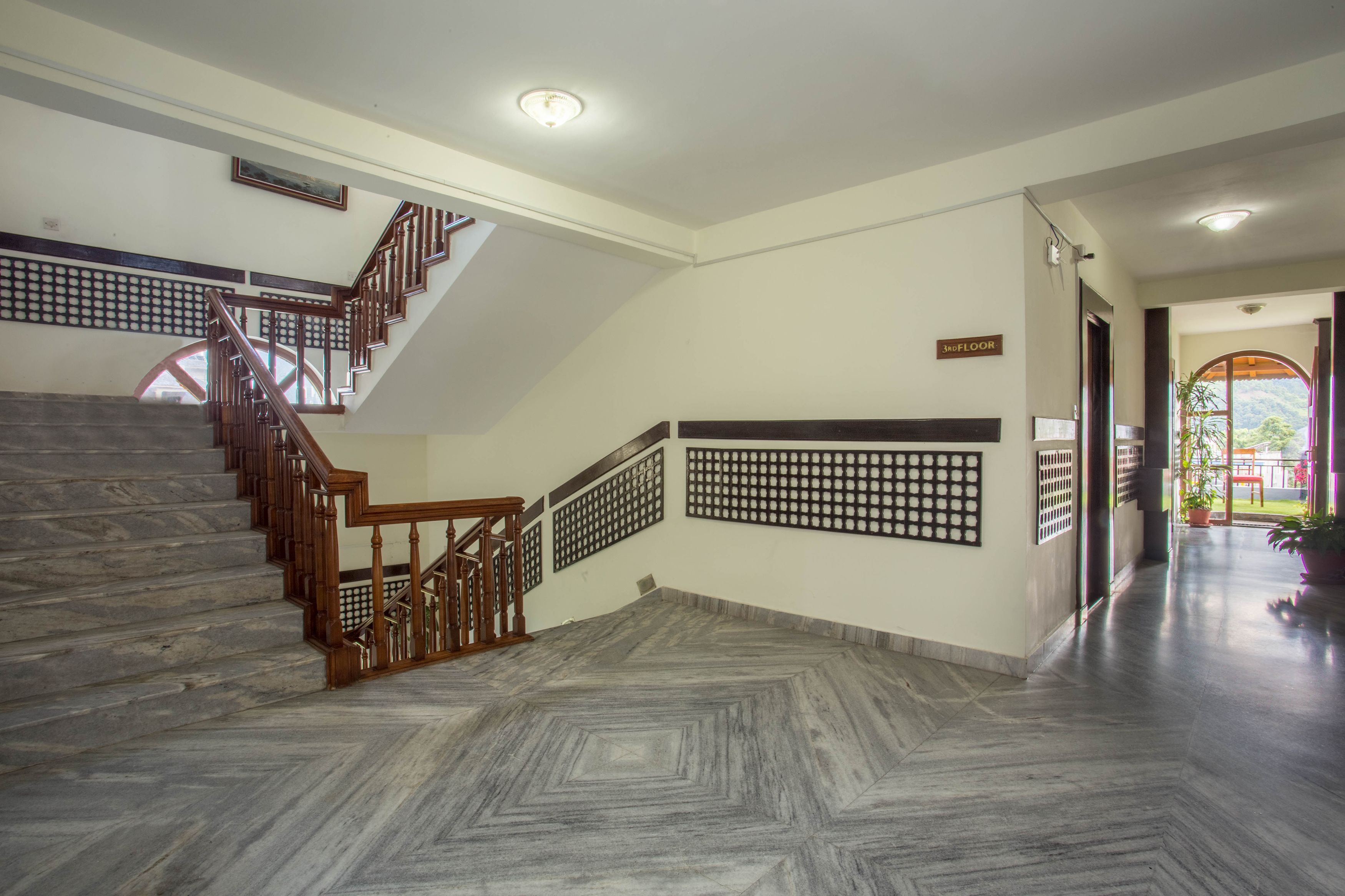 Vestíbulo de hotel con una escalera de mármol, mostrador de recepción y vista al exterior.
