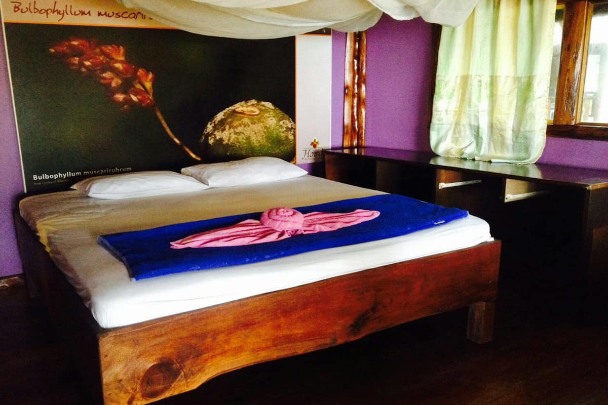 Una cama con una manta azul y una toalla rosa, un cabecero de madera, una pared con un póster y una ventana con cortinas.