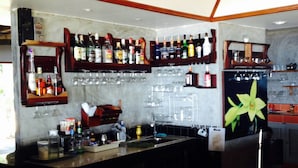 A bar area with shelves of liquor bottles, glasses, and a wooden bar counter.