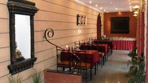 A restaurant with wooden panel walls, a fireplace, and tables set with red tablecloths. - Hotel Shakti (Kathmandu)