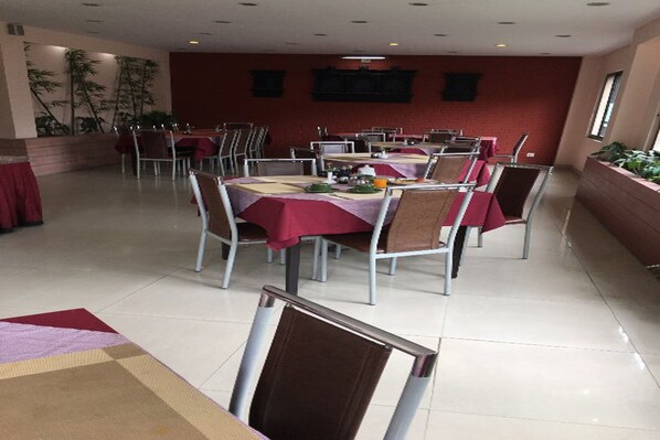 Un comedor con mesas dispuestas para cuatro, cada una con mantel rojo y sillas de metal.