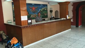 A reception desk with a wooden finish, a large mural on the wall, and a tiled floor. - Hotel Shakti (Kathmandu)