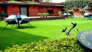 A red building with a green lawn, outdoor seating, and a stone with "STANFORD" engraved. - Hotel Shakti (Kathmandu)