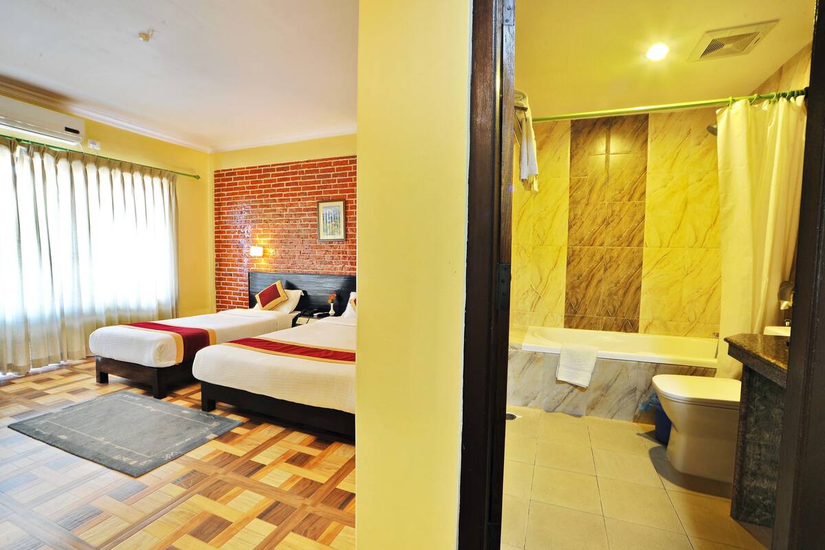 A hotel room with two beds, a brick wall, a bathroom with a bathtub, and a tiled floor.