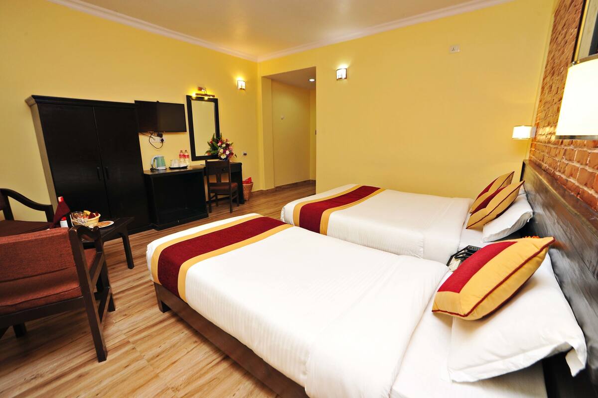 A hotel room with two beds, a desk, a chair, and a television.