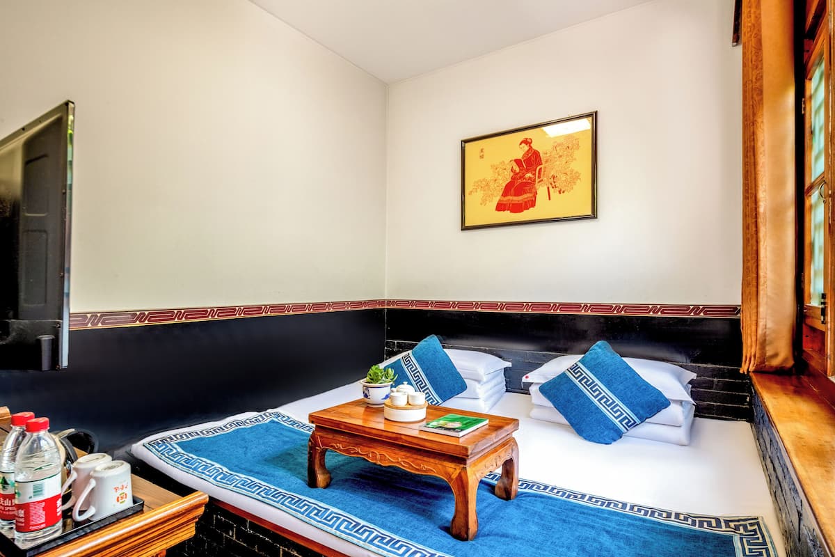A neatly arranged room with a bed, pillows, a small table with a plant, and a framed picture on the wall.