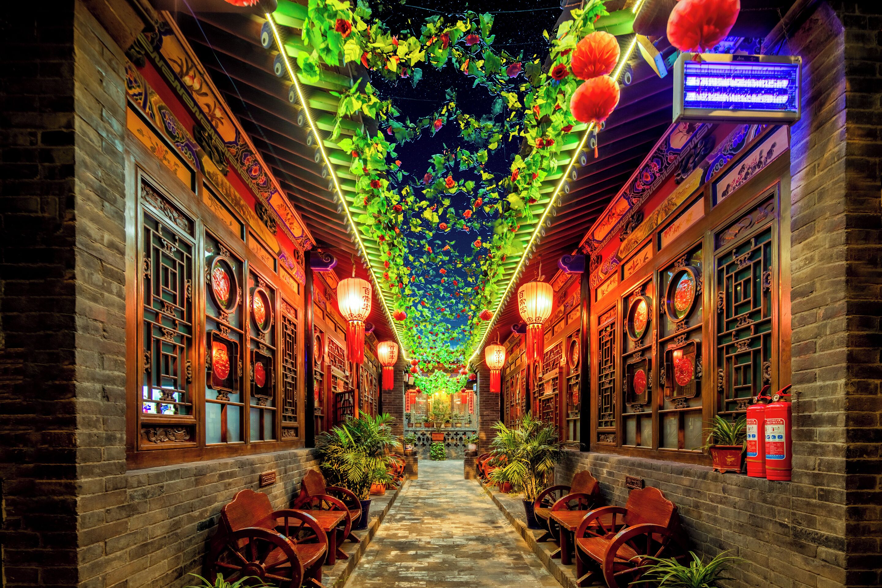 A corridor with traditional Chinese architecture, including wooden doors and windows, and a ceiling adorned with hanging lanterns and decorative elements.