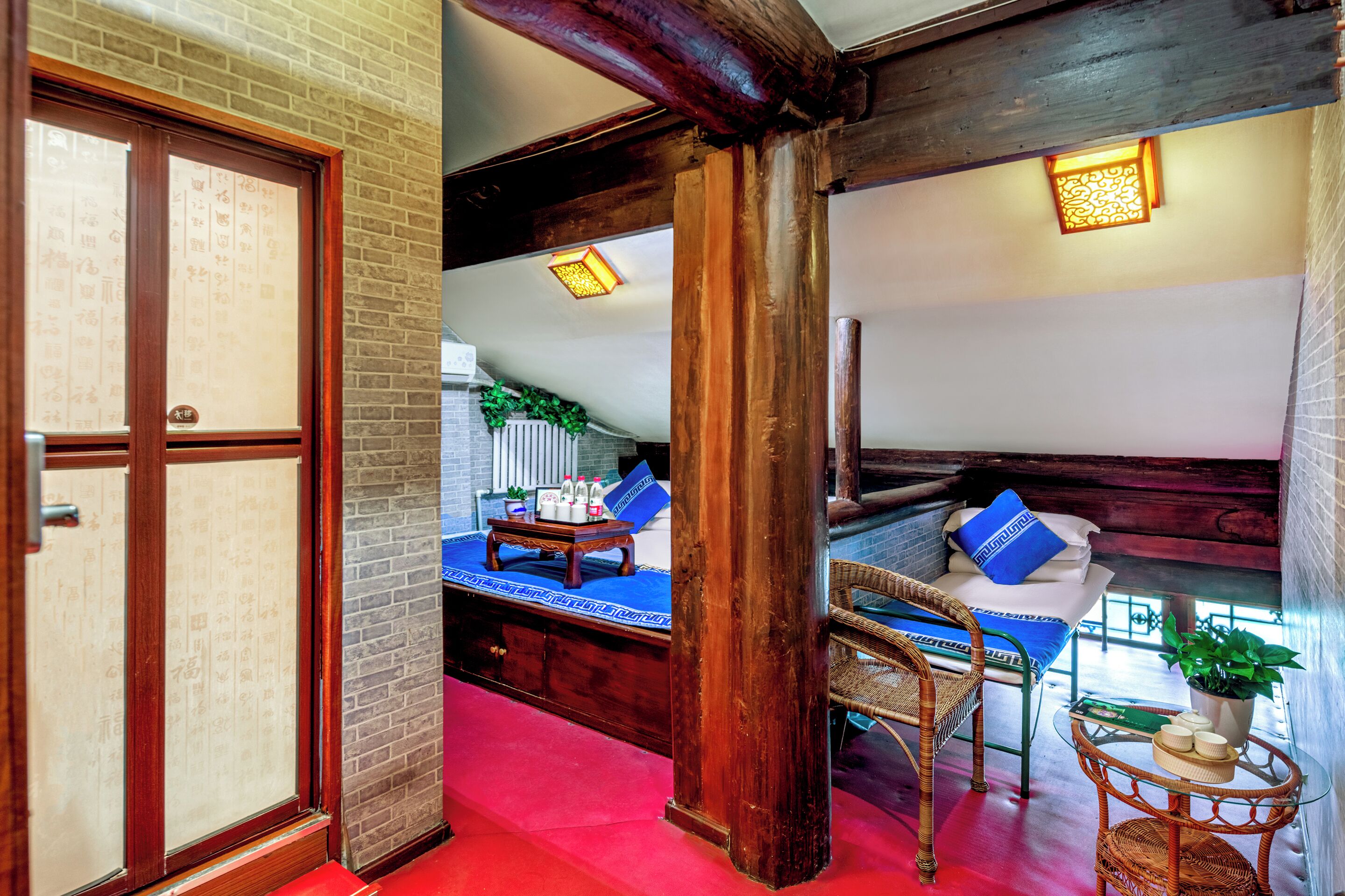 A traditional Japanese-style room with tatami flooring, a low wooden bed with blue cushions, a small table with a plant, and a sliding door with calligraphy.
