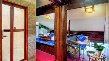 A traditional Japanese-style room with tatami flooring, a low wooden bed with blue cushions, a small table with a plant, and a sliding door with calligraphy.