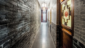 Un corridoio stretto con pareti in mattoni, una porta in legno decorata con motivi tradizionali cinesi e un lampadario sospeso.