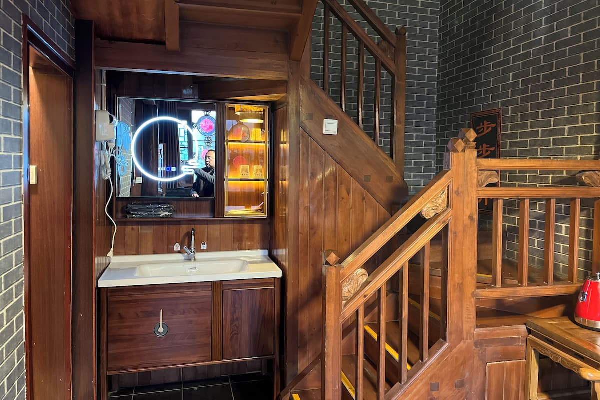 A wooden staircase with a handrail, a wooden door, and a mirror with a circular light.