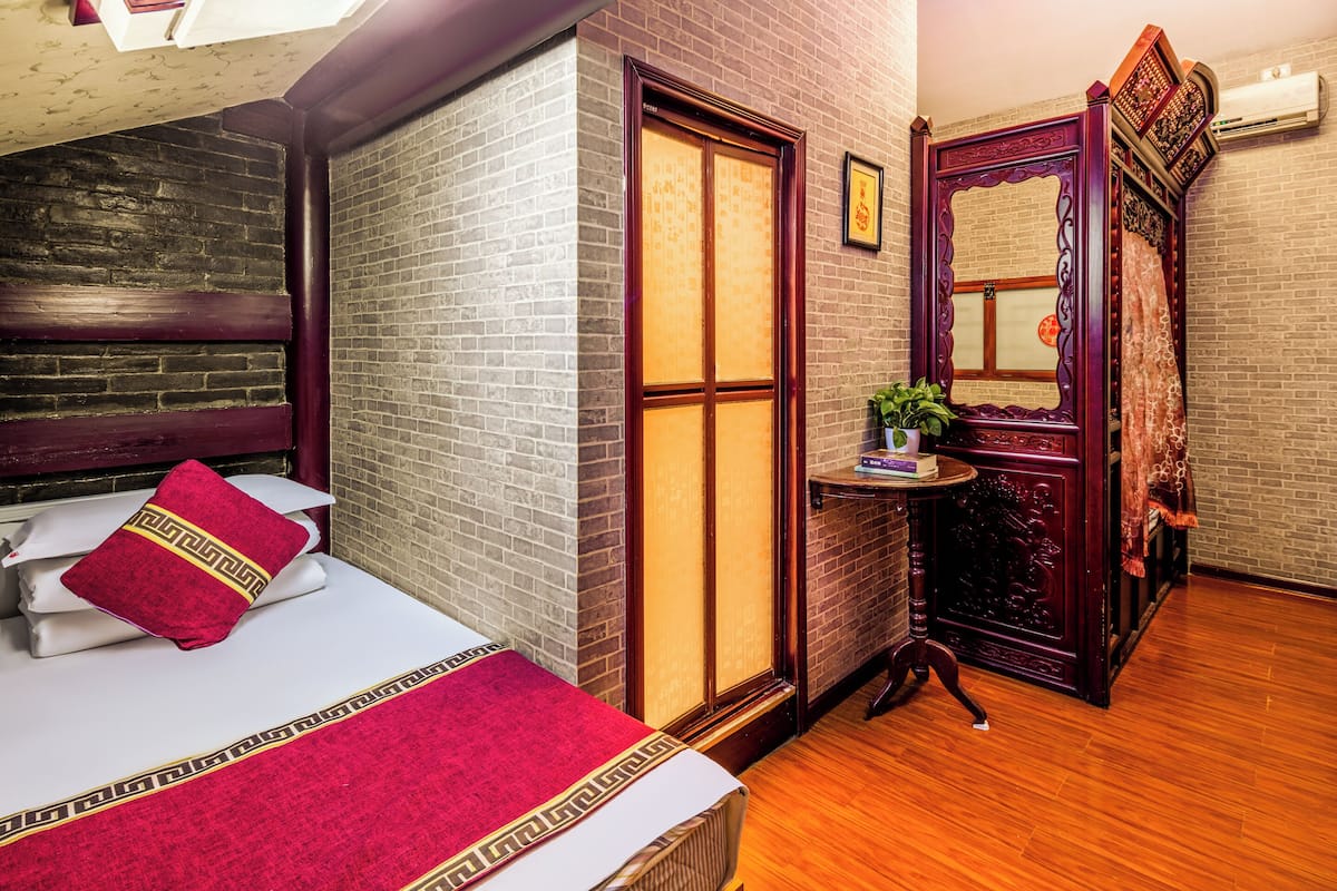 A hotel room with a bed, a small table with a plant, and a traditional wooden wardrobe.