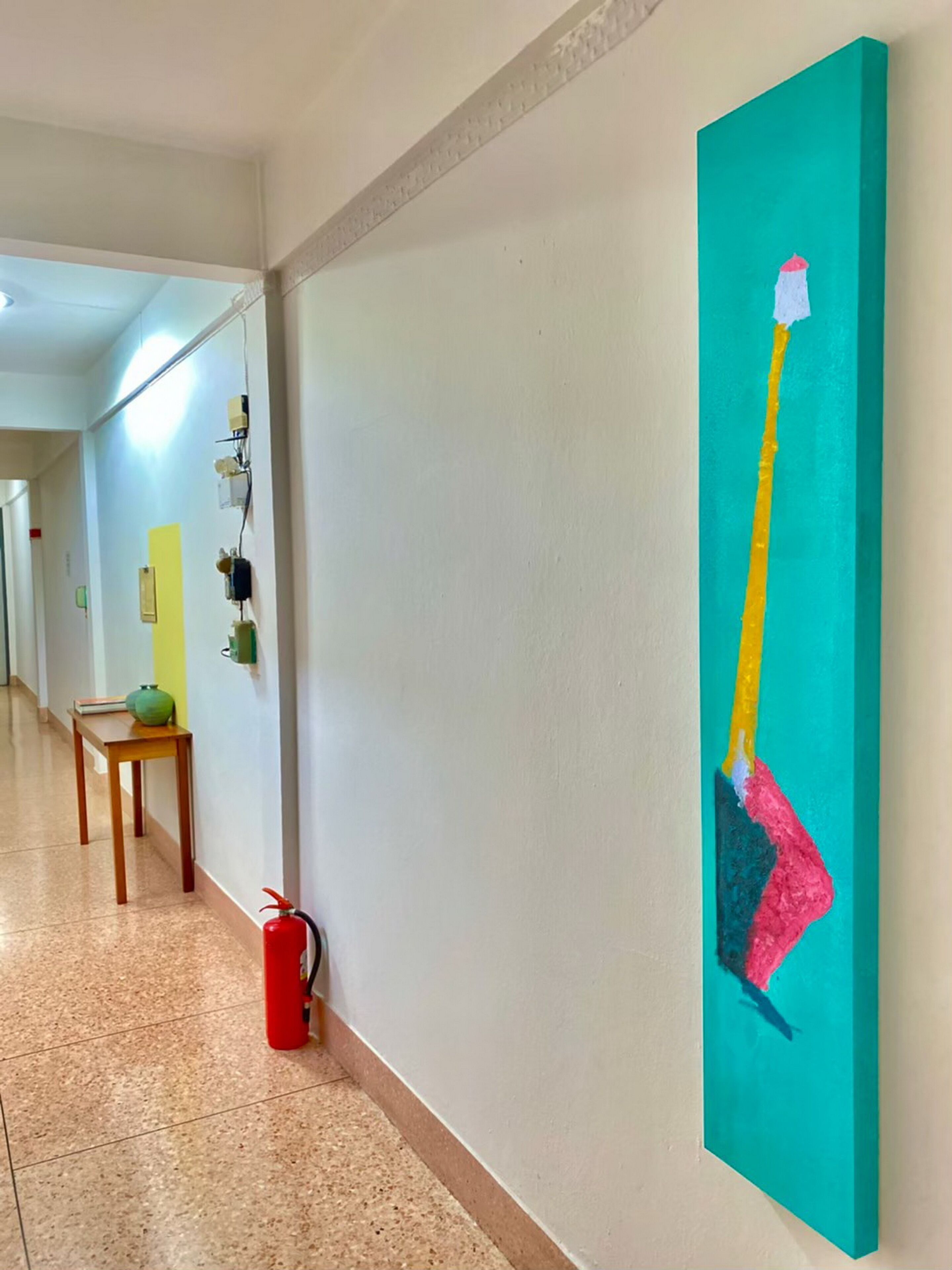 A hallway with a fire extinguisher, a table with a vase, and a painting on the wall.