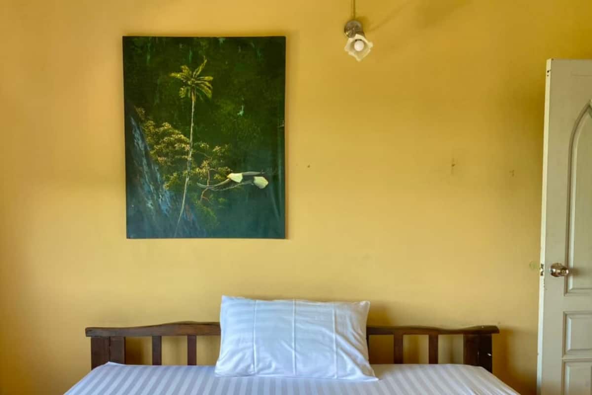Un lit avec une couvre-lit rayée blanche et bleue et une couverture bleue à texture, un oreiller blanc et un tableau représentant un arbre aux fleurs blanches sur un mur jaune.