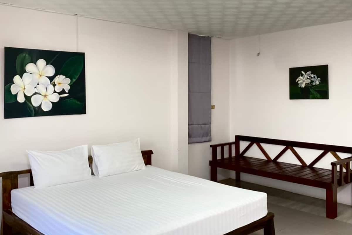 Une chambre avec un lit en bois, une literie blanche, un banc et deux œuvres d’art florales accrochées au mur.