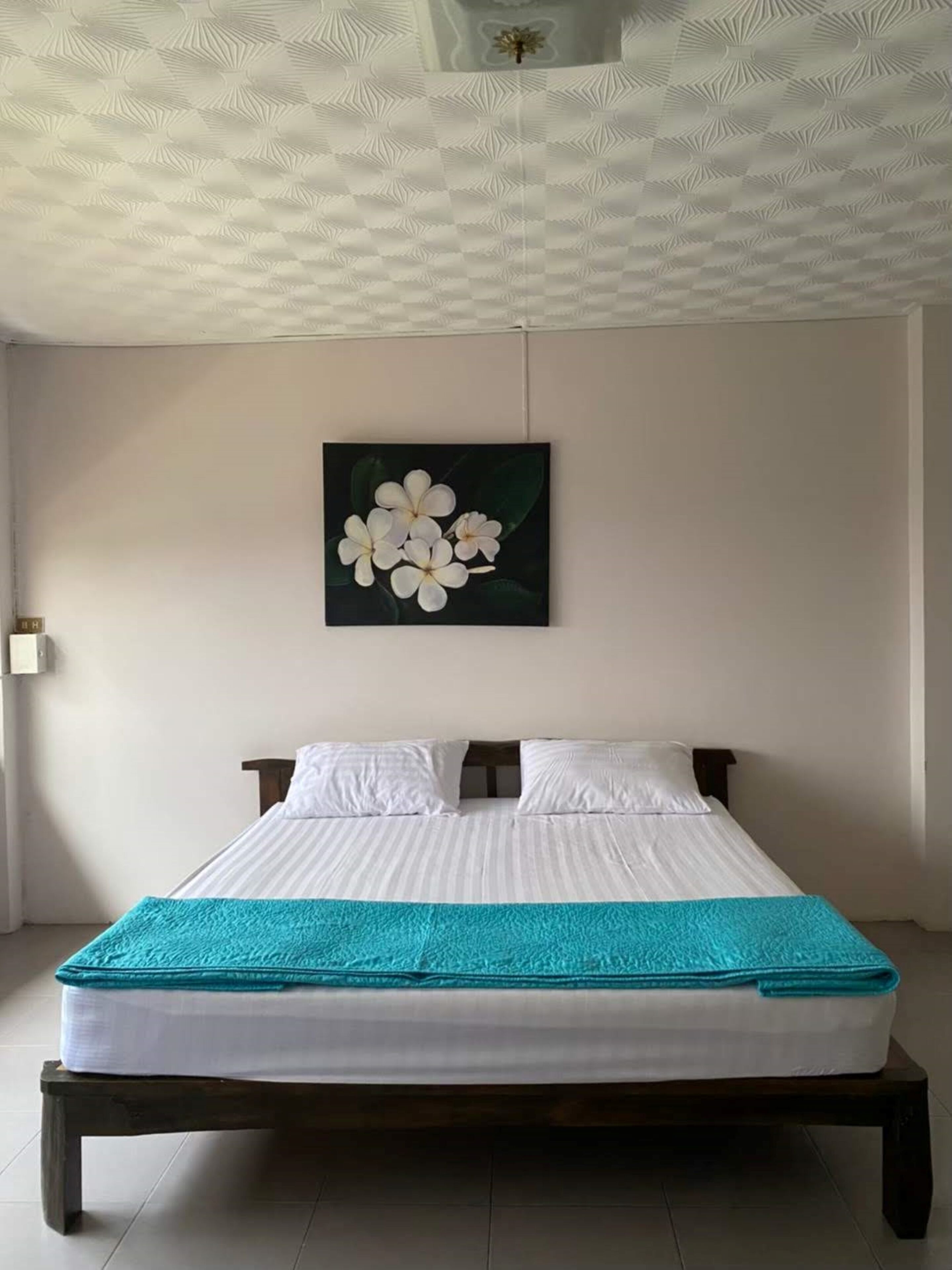Un lit bien fait, avec une couverture turquoise, un oreiller blanc et une tête de lit en bois foncé.