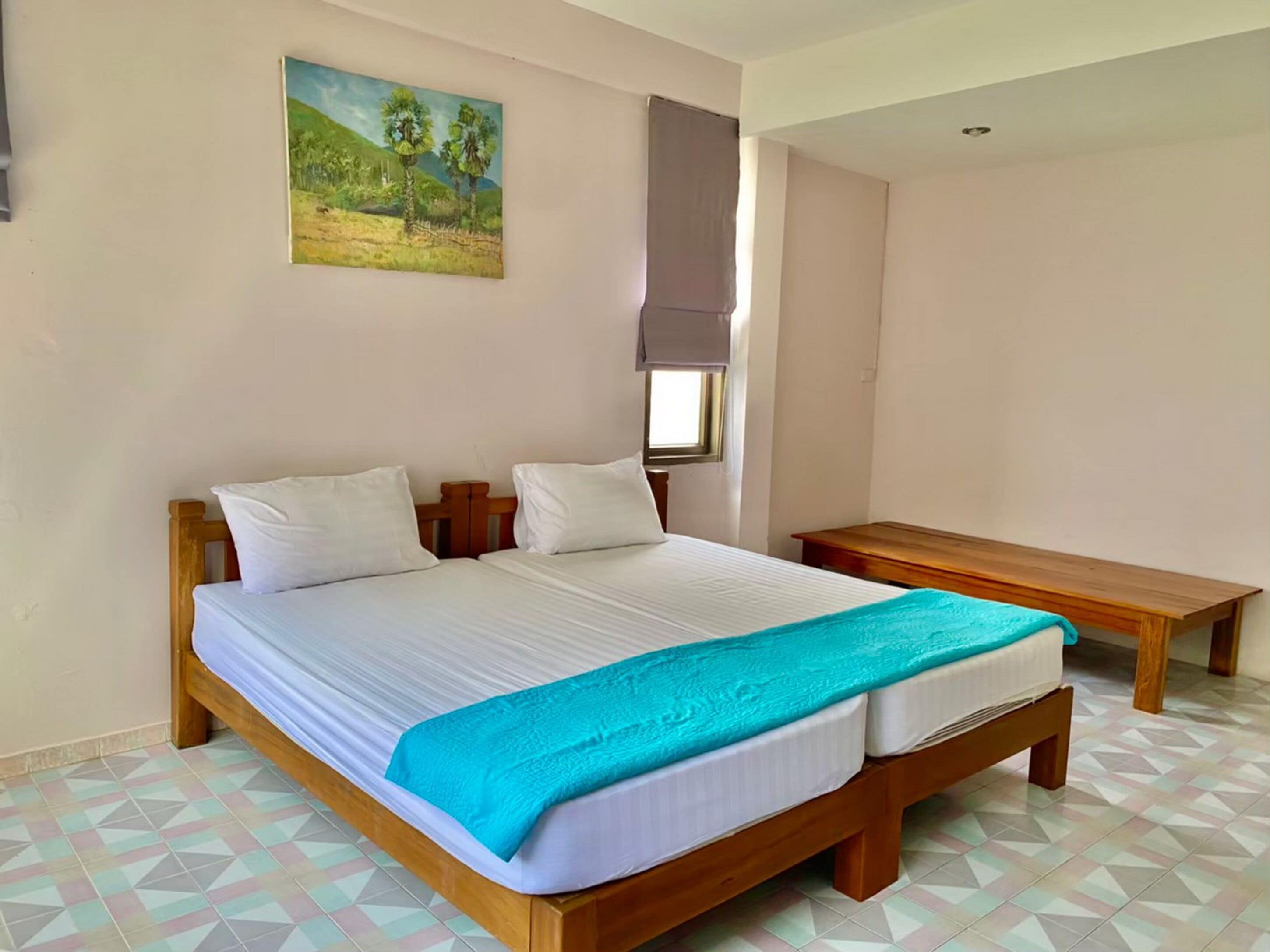Un dormitorio con una cama, una mesita de noche de madera, un cuadro en la pared y una ventana con cortina.