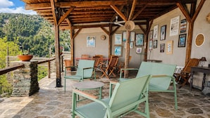 A rustic outdoor seating area with stone flooring, wooden furniture, and a mountain backdrop.