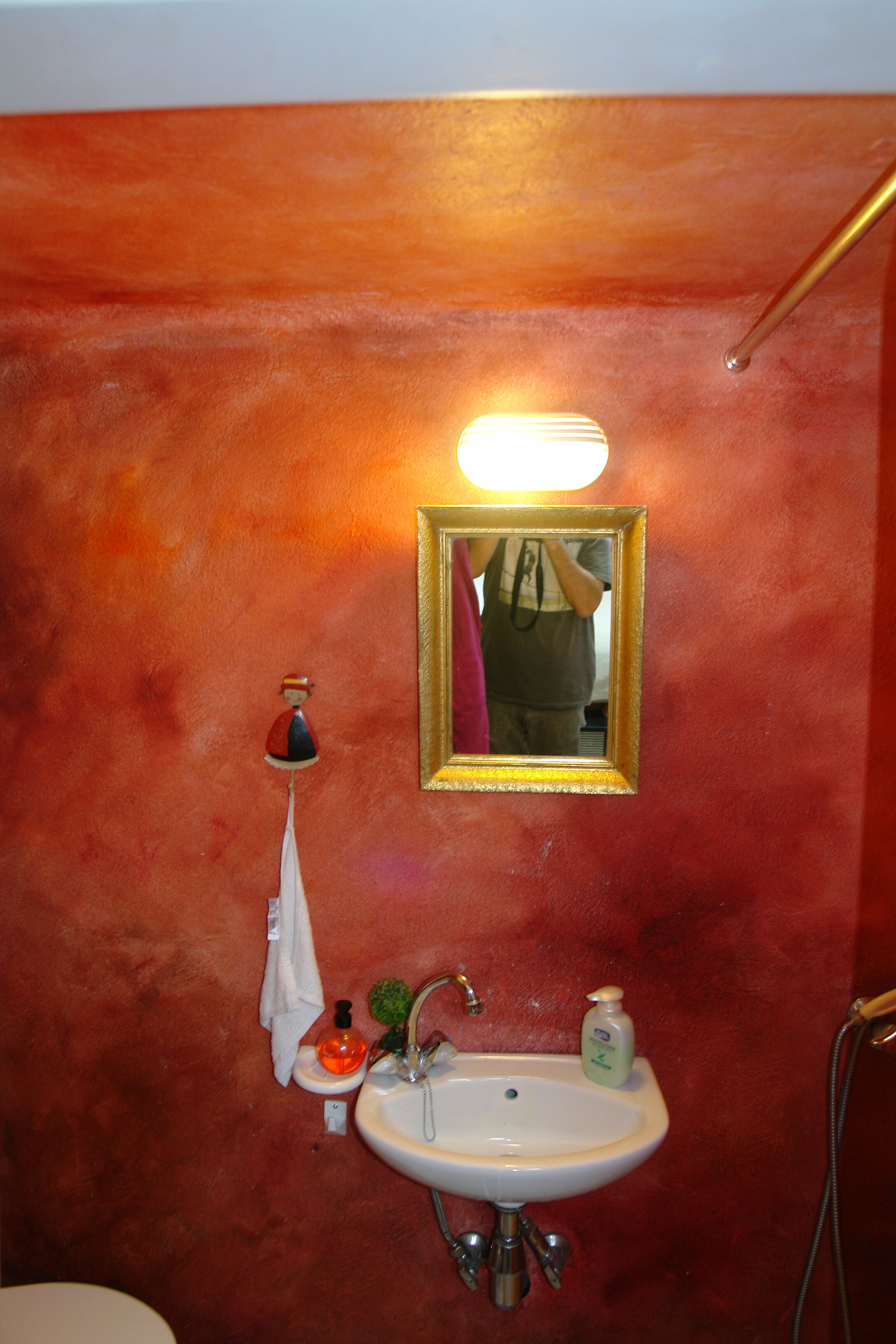 A bathroom with a red wall, a white sink, a mirror, and a towel hanging on the wall.